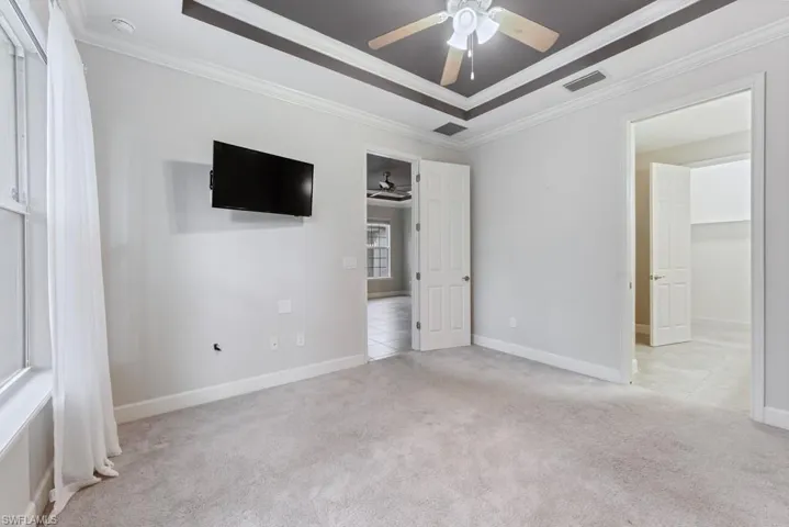 Primary bedroom with crown molding, ceiling fan, light carpet, and a tray ceiling