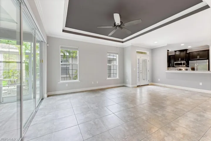 Unfurnished living room featuring crown molding, light tile patterned flooring, a tray ceiling, and ceiling fan