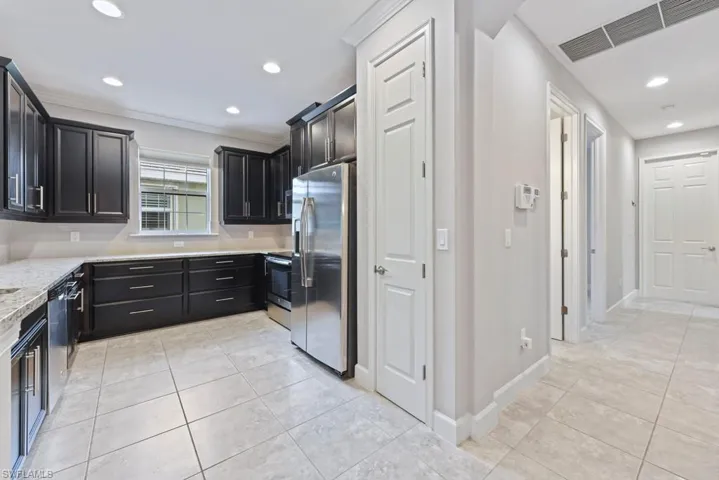 Kitchen with light stone counters, stainless steel appliances, crown molding, and light tile patterned flooring