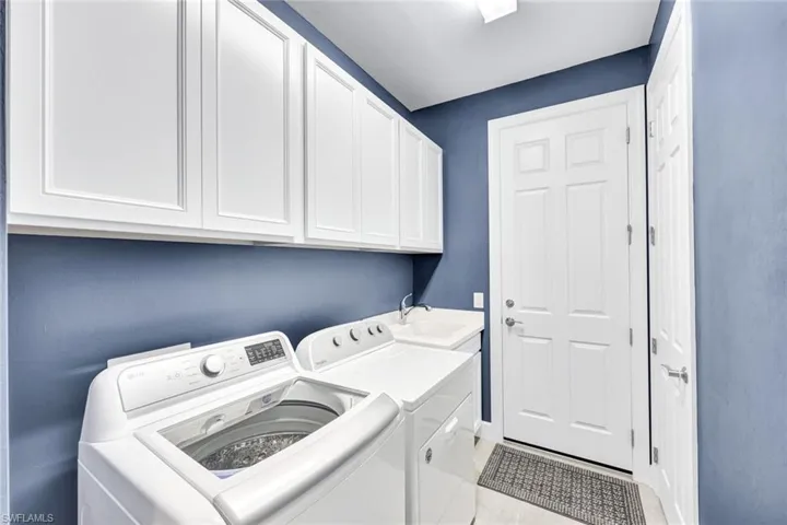 Clothes washing area featuring light tile patterned flooring, cabinets, independent washer and dryer, and sink