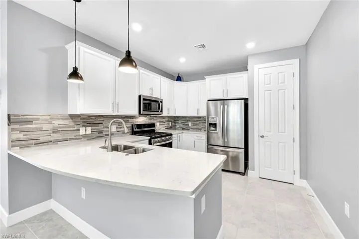 Kitchen featuring pendant lighting, stainless steel appliances, kitchen peninsula, sink, and white cabinets