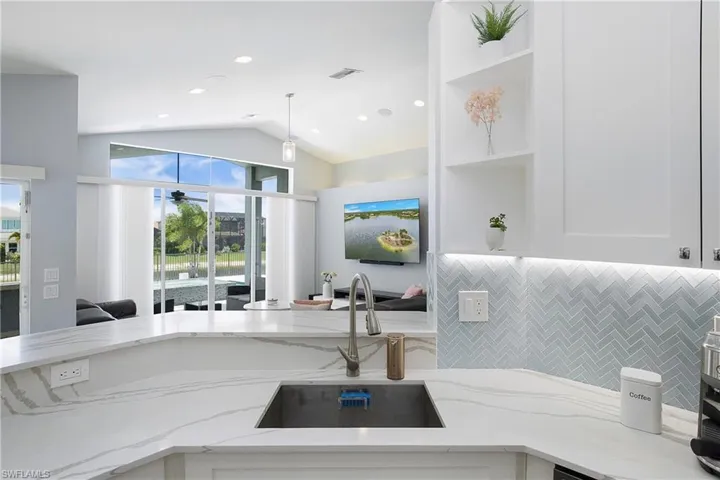 Kitchen featuring light stone countertops, sink, white cabinets, and lofted ceiling