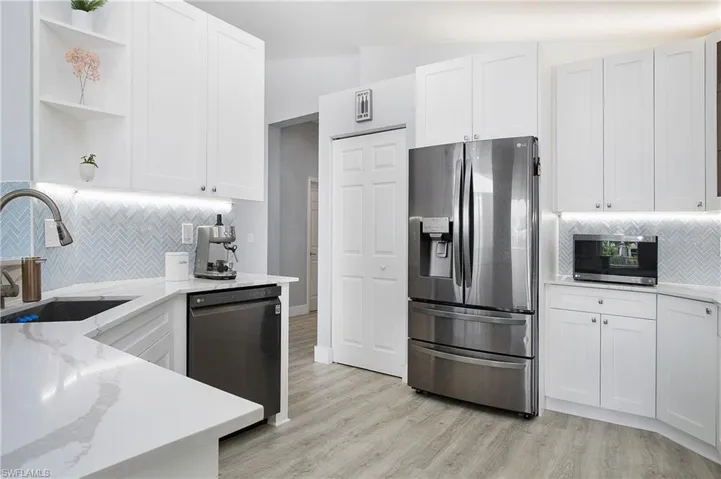Kitchen featuring light stone counters, stainless steel appliances, sink, white cabinets, and lofted ceiling