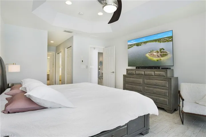 Bedroom with ceiling fan, light hardwood / wood-style flooring, and a tray ceiling