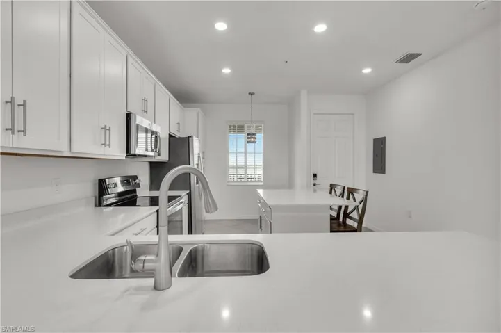White shaker-style cabinetry, stainless steel appliances, recessed lighting, and a kitchen island with seating