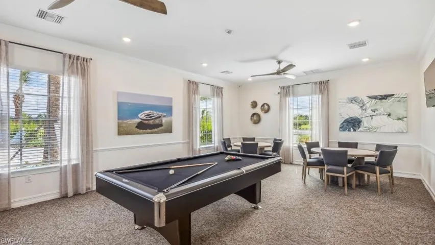 This spacious room features a pool table, round tables with chairs, and large windows with blinds