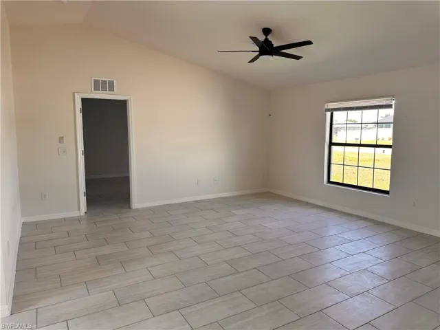 Empty room with vaulted ceiling, baseboards, visible vents, and ceiling fan