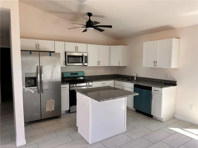 Kitchen with a kitchen island, ceiling fan, stainless steel appliances, vaulted ceiling, and white cabinets