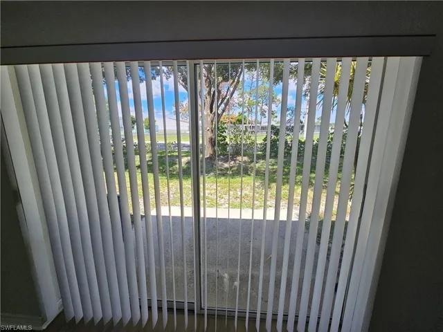 Sliding glass door with vertical blinds offering access to an outdoor patio area and expansive lawn