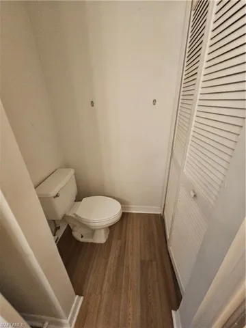 Compact restroom featuring a white toilet, wood-finish flooring, white baseboards, and louvered bifold doors