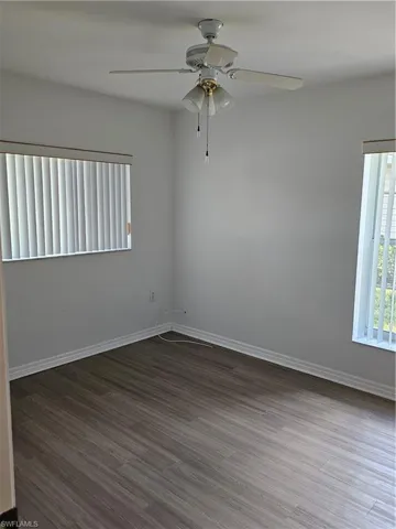 Neutral toned room with wood-finish flooring, white walls, and a ceiling fan with integrated lighting