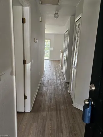 Hallway featuring wood-finish flooring, white walls, and built-in closet storage with louvered doors