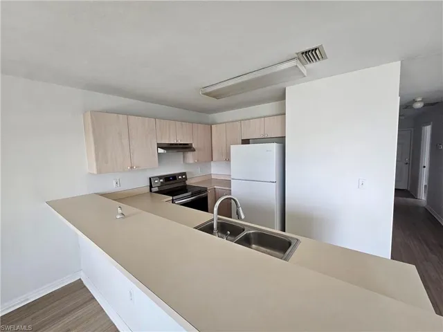 Kitchen featuring a double basin stainless steel sink with pull-down faucet, light wood-finish cabinetry, and a black electric range with coordinating range hood