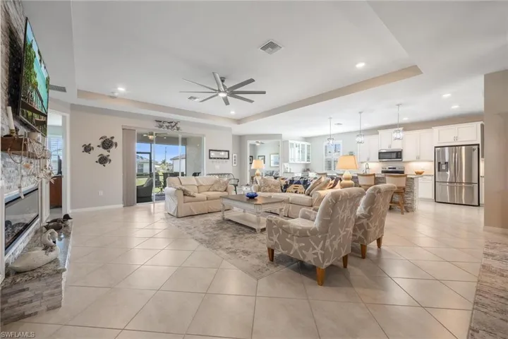 Tiled living room with a fireplace, ceiling fan with notable chandelier, and a tray ceiling