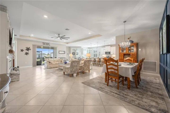 Tiled dining room featuring ceiling fan with notable chandelier and a raised ceiling