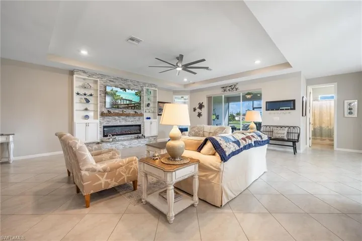 Living room featuring ceiling fan, a raised ceiling, light tile patterned floors, and a fireplace