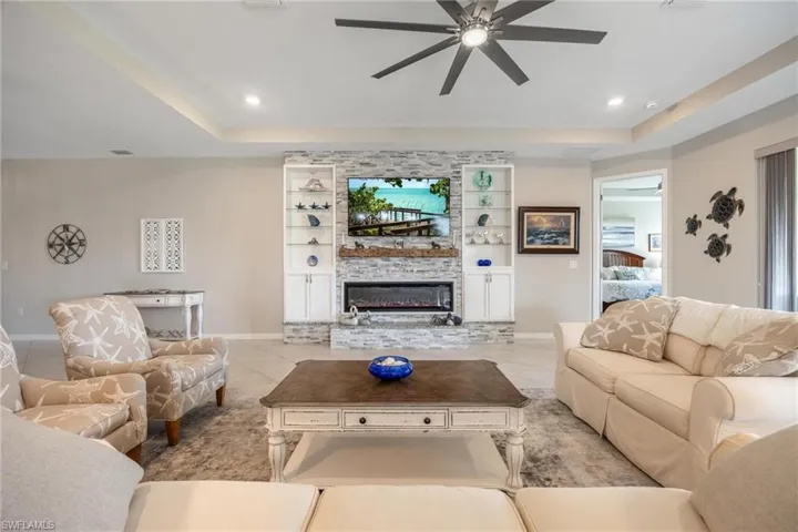 Living room with a tray ceiling, a stone fireplace, ceiling fan, and light tile patterned flooring