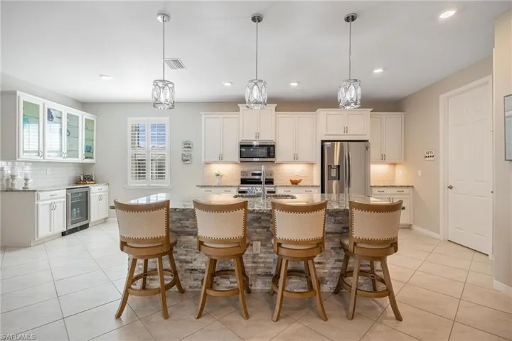Kitchen with light stone countertops, an island with sink, beverage cooler, and stainless steel appliances