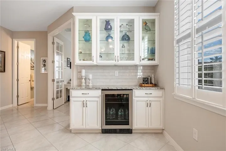 Bar with decorative backsplash, plenty of natural light, white cabinets, and beverage cooler