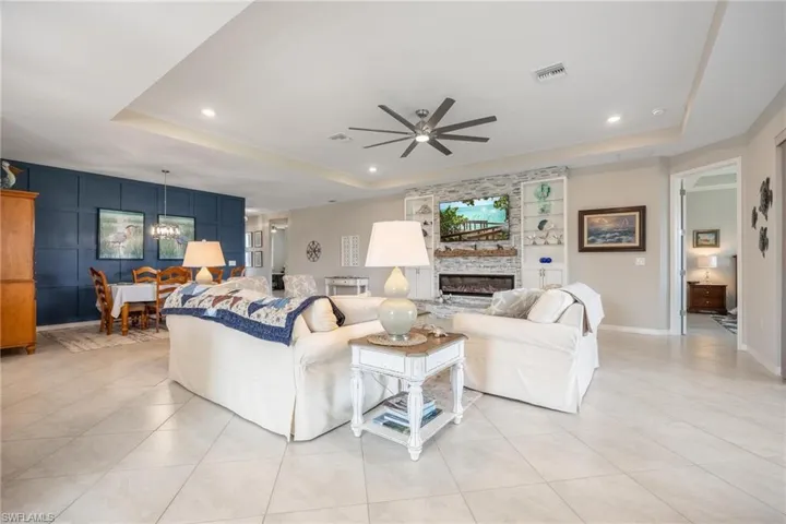 Tiled living room with ceiling fan with notable chandelier, a fireplace, and a tray ceiling