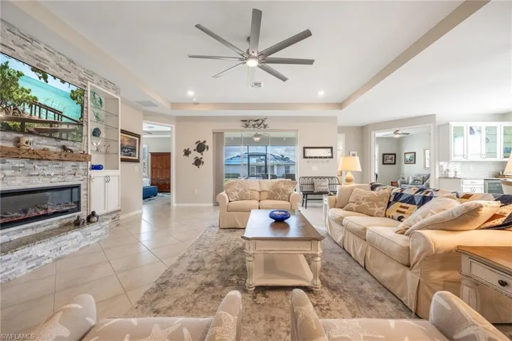 Living room with a fireplace, light tile patterned floors, a raised ceiling, and ceiling fan