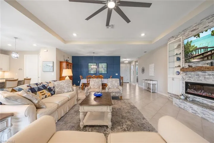Tiled living room with ceiling fan with notable chandelier, a healthy amount of sunlight, a stone fireplace, and a tray ceiling