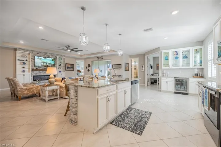Kitchen featuring a kitchen island with sink, white cabinets, wine cooler, light stone countertops, and stainless steel appliances
