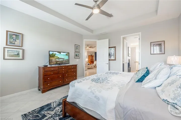Tiled bedroom with a tray ceiling, ensuite bathroom, and ceiling fan