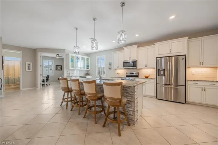 Kitchen featuring hanging light fixtures, light stone countertops, an island with sink, appliances with stainless steel finishes, and a kitchen bar
