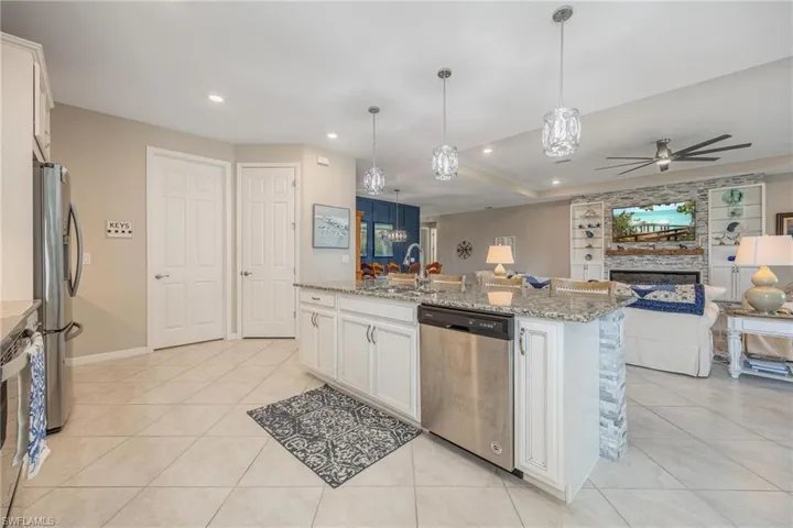 Kitchen with white cabinets, decorative light fixtures, stainless steel appliances, and a center island with sink