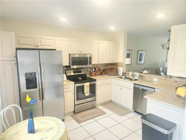 Kitchen featuring kitchen peninsula, stainless steel appliances, sink, white cabinetry, and light stone counters