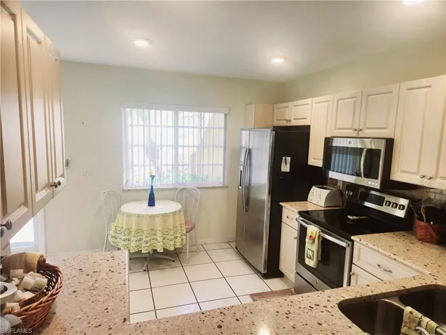 Kitchen with white cabinetry, light stone counters, appliances with stainless steel finishes, and light tile patterned floors