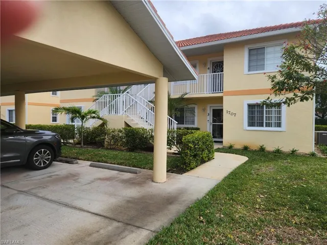 View of front of house with central air condition unit, a balcony, and a front lawn