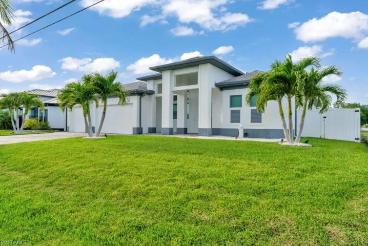 The property features a modern white exterior with a dark grey roof, a lush green lawn, and several mature palm trees