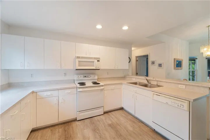 Kitchen featuring light hardwood / wood-style flooring, white appliances, kitchen peninsula, pendant lighting, and sink