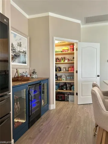 Bar area with ornamental molding, light wood-style flooring, wine cooler, and stainless steel fridge