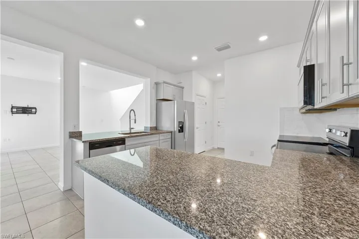 Kitchen featuring a peninsula, light tile patterned floors, dark stone countertops, stainless steel appliances, and tasteful backsplash