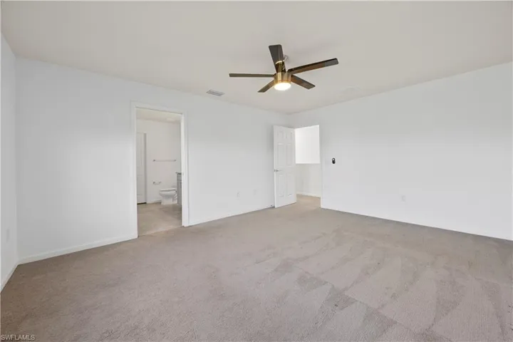 Unfurnished bedroom featuring light colored carpet, ceiling fan, and ensuite bathroom