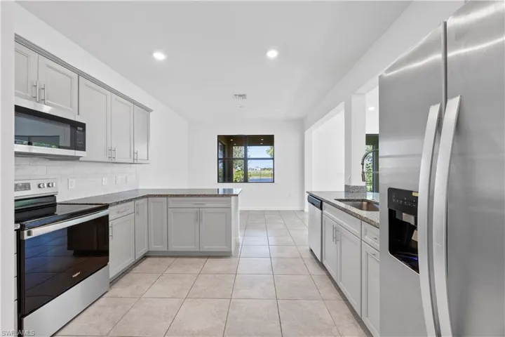 Kitchen with stainless steel appliances, a peninsula, light stone counters, backsplash, and light tile patterned flooring