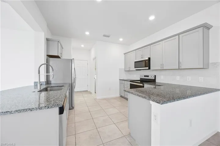 Kitchen featuring dark stone counters, appliances with stainless steel finishes, backsplash, a peninsula, and light tile patterned floors