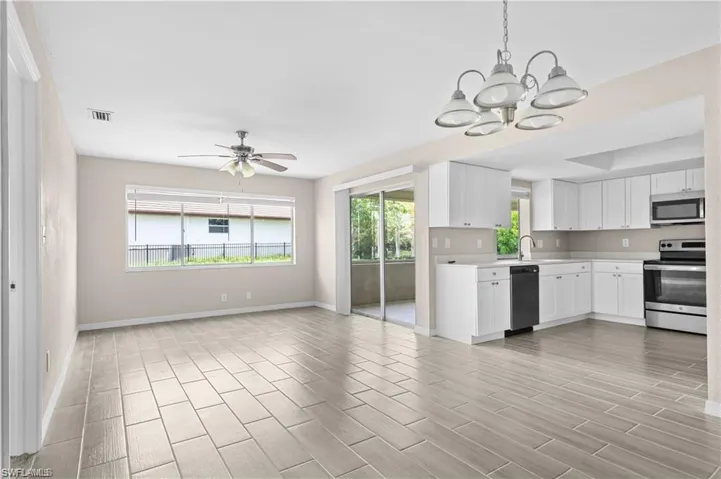 Kitchen featuring appliances with stainless steel finishes, light countertops, white cabinets, hanging light fixtures, and wood tiled floors