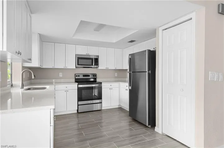 Kitchen with stainless steel appliances, light stone counters, white cabinets, wood finish floors, and a raised ceiling