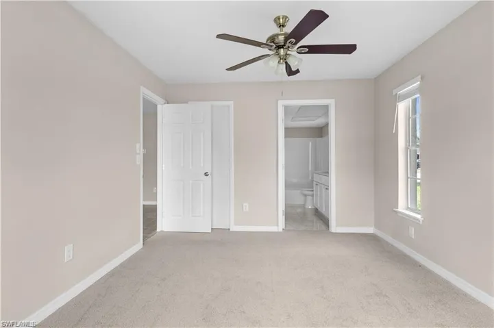 Unfurnished bedroom with light colored carpet, ensuite bath, and ceiling fan