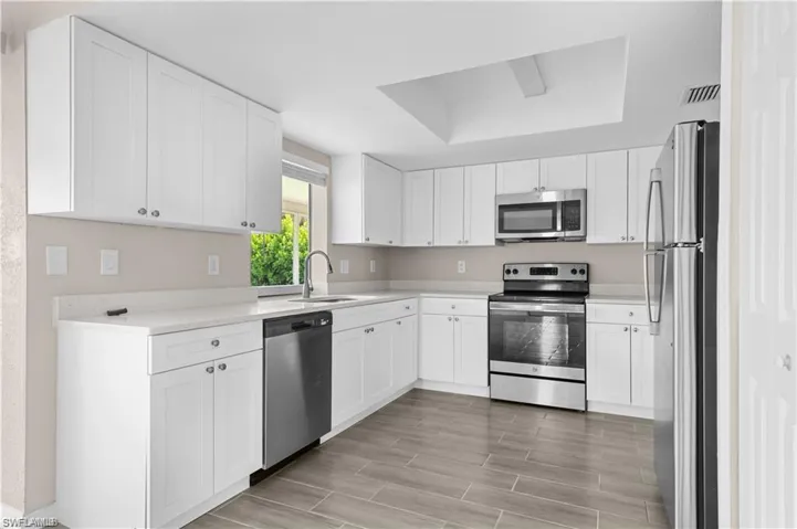 Kitchen with stainless steel appliances, white cabinets, wood finish floors, a raised ceiling, and light stone countertops