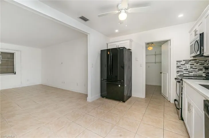 Kitchen featuring stainless steel appliances, a ceiling fan, light tile patterned flooring, decorative backsplash, and white cabinets