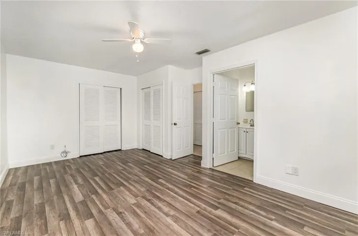 Unfurnished bedroom featuring wood finished floors, ensuite bath, multiple closets, and ceiling fan