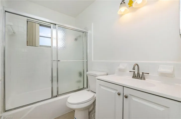 Full bath featuring vanity, bath / shower combo with glass door, tile walls, and wainscoting