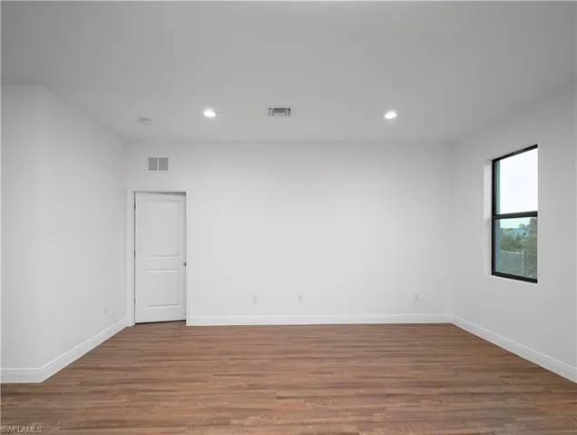 Wood-finish flooring, recessed lighting, white walls, two-panel interior door, and black-framed window