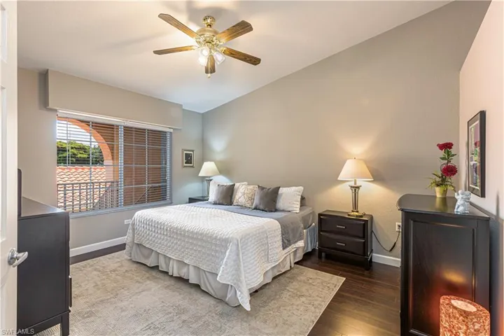 Vaulted ceiling bedroom with wood-finish flooring, a window with horizontal blinds, and a brass-finish ceiling fan