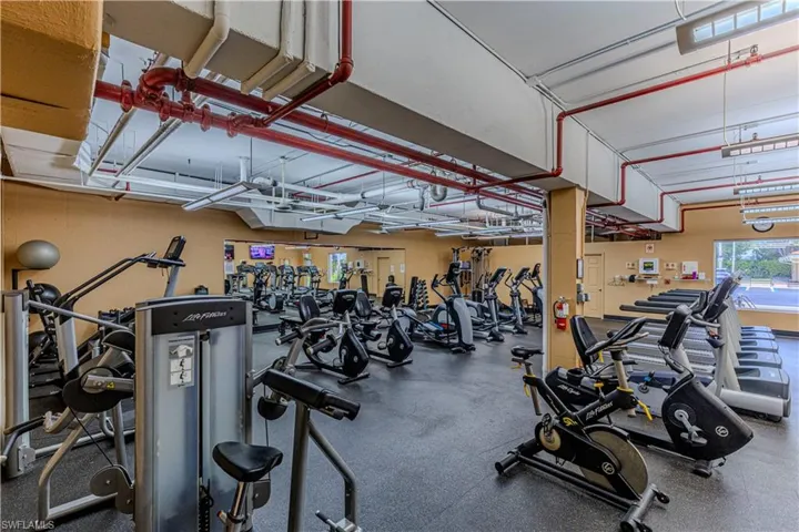 Fitness center featuring extensive cardio equipment, strength training machines, mirrored walls, rubberized flooring, and exposed ceiling ductwork